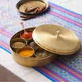a golden brass masala dabba spice tin with lid slightly open showcasing multiple spices in several compartments